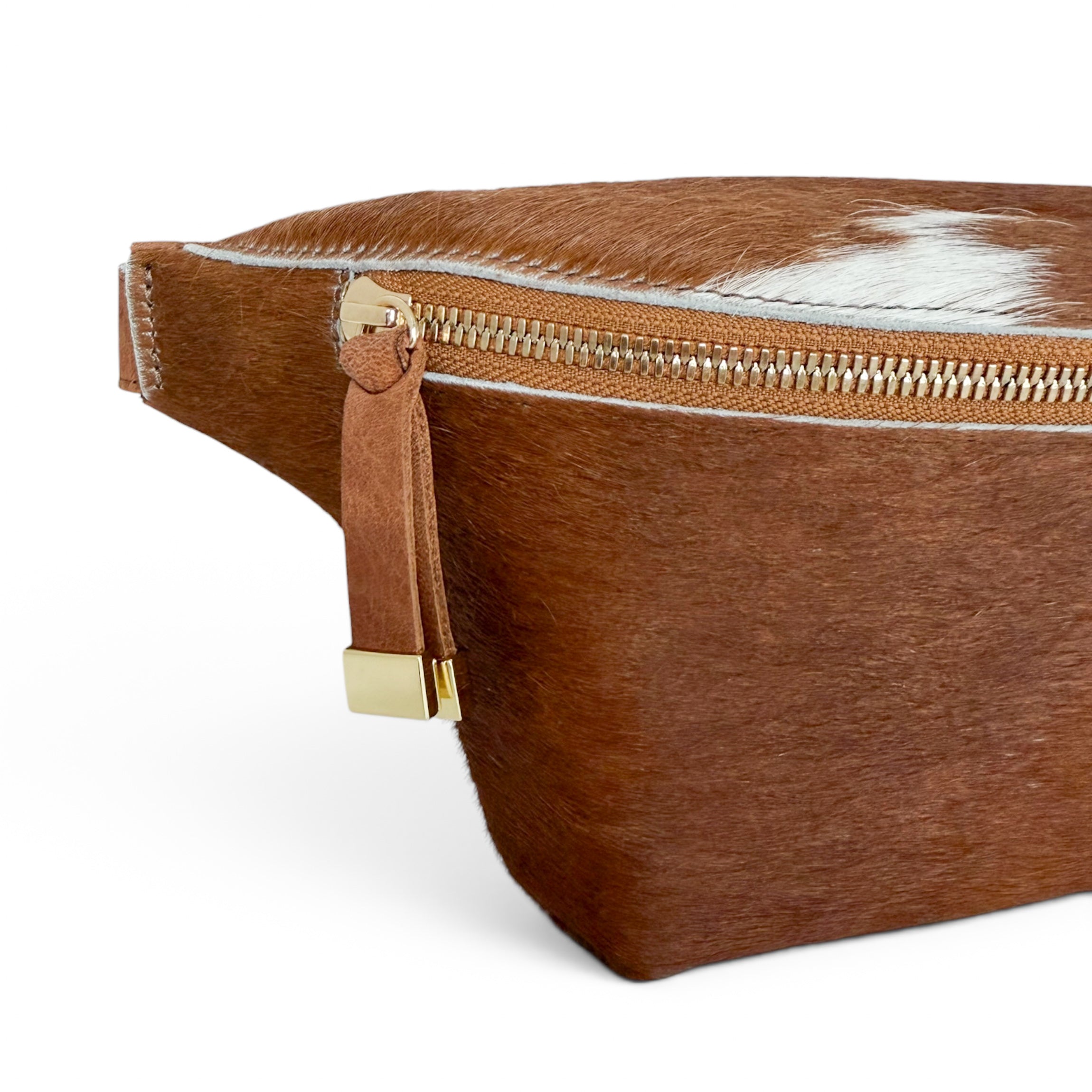 Close-up of a brown faux-hair or hair-on-hide bag with a gold-tone zipper and leather pull tab, shown on a clean white background.